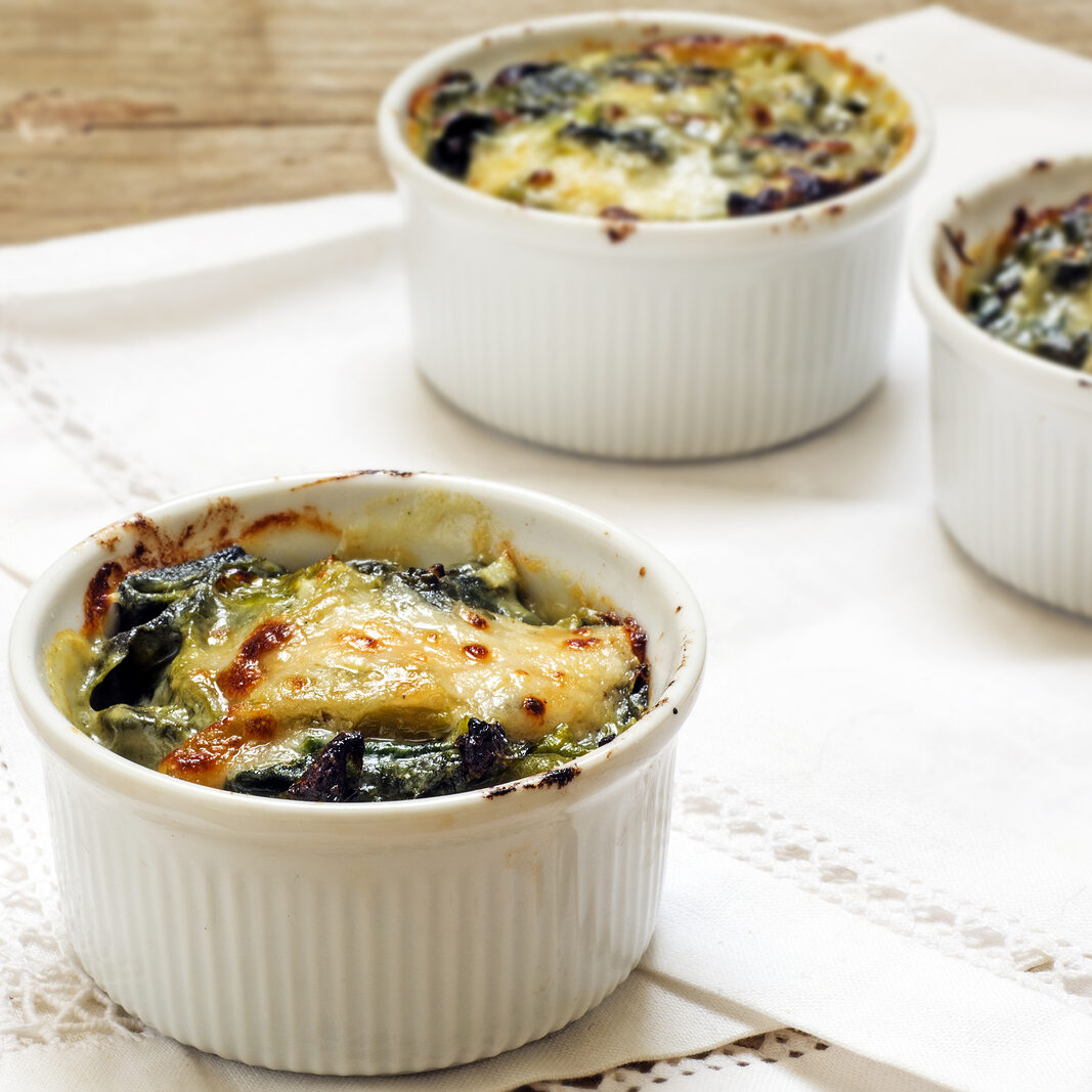 baked spinach with cheese in small casserole servings white napkin on a rustic wooden table selected focus narrow depth of field